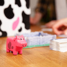 Pink cow-shaped toy on a wooden table with game components in the background
