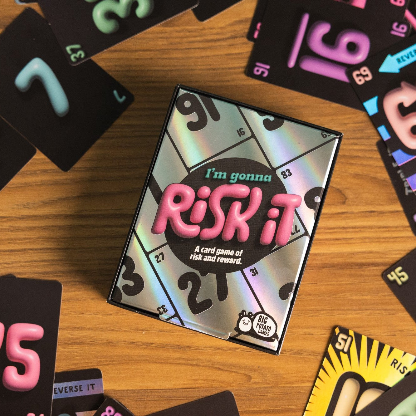 Risk it card game packaging surrounded by colorful cards on a wooden surface