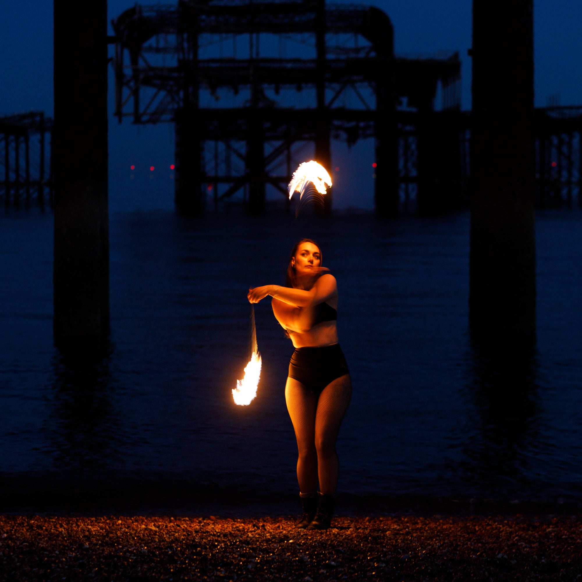 Person spinning fire poi on the beach at night