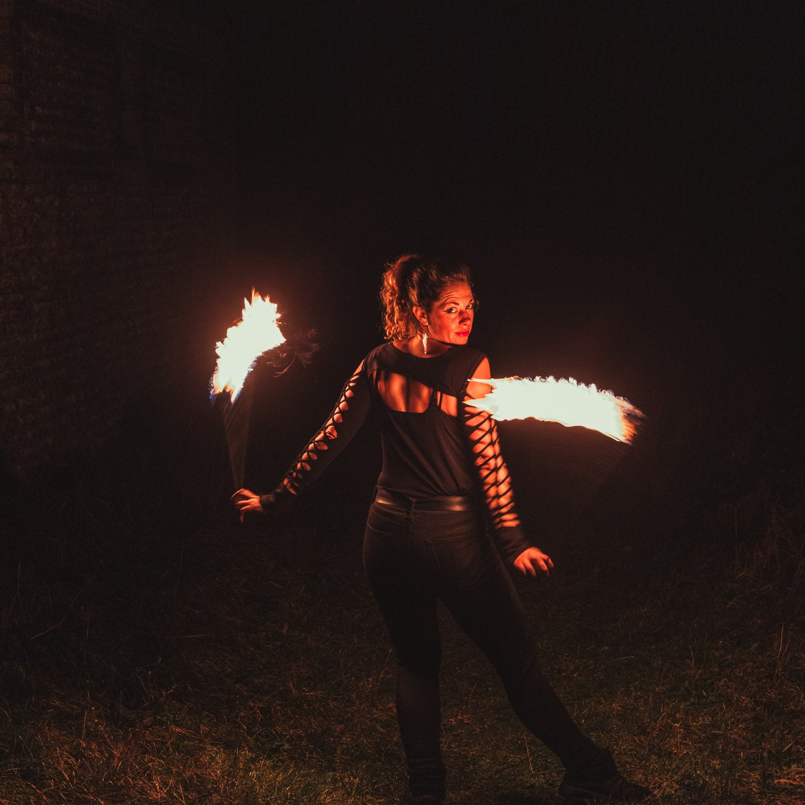 a photo of a woman spinning cathedral fire poi at night, facing away from the camera