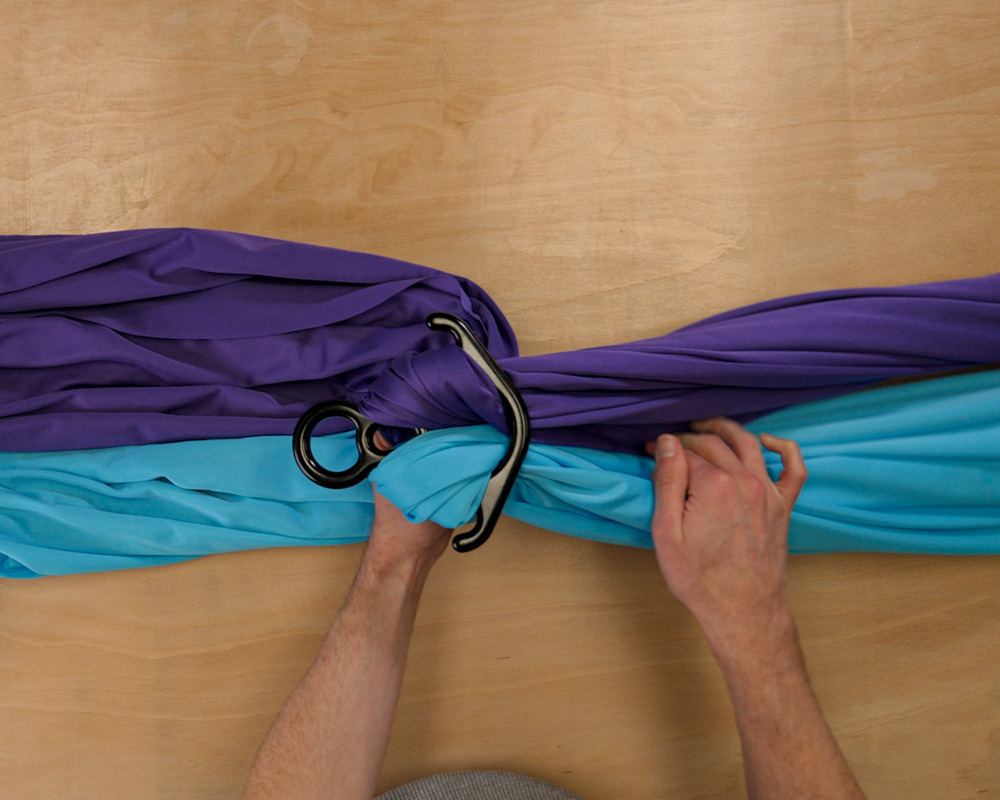 A purple silk and a blue aerial silk on a table threaded through a figure 8 rigging accessory by hand and then looped over the top of the figure 8