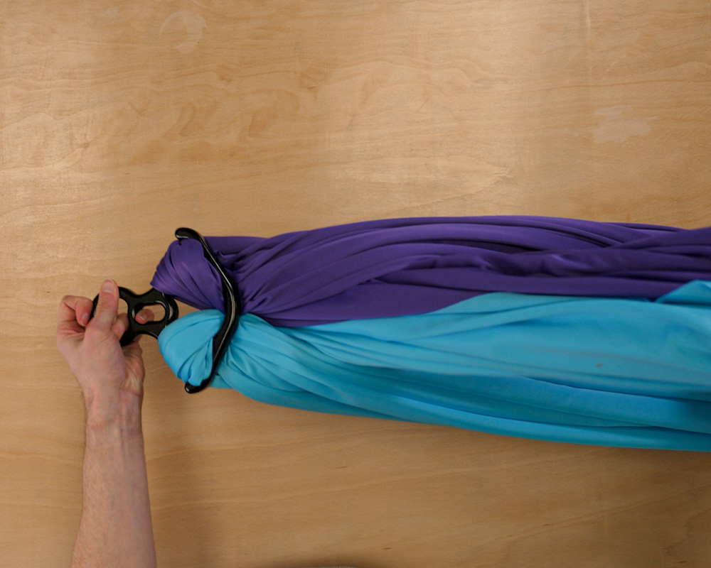 A purple silk and a blue aerial silk on a table being held by the top of the figure 8 rigging accessory